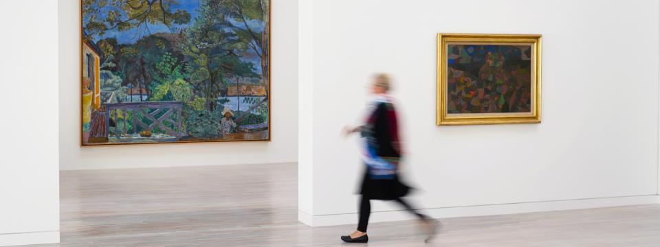 Eine Frau läuft in der Kunstsammlung an Gemälden vorbei.