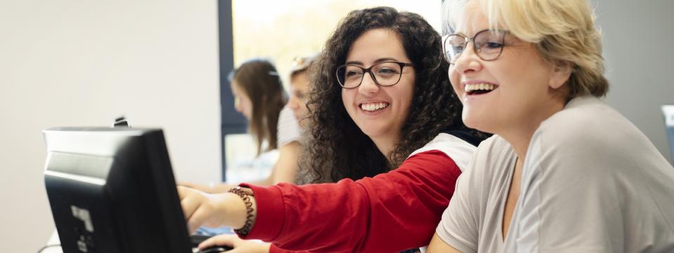 Eine jüngere und eine ältere Frau am Computer, die jüngere Frau zeigt der anderen etwas