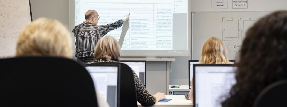 Eine Unterrichtsstunde, mehrere Menschen hören einem Lehrer zu, der etwas erläutert