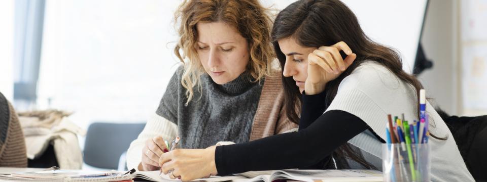 Zwei Frauen an einem Tisch, die eine zeigt der anderen etwas