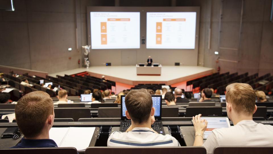 Drei männliche Studenten im Hörsaal mit Laptop und Tablet