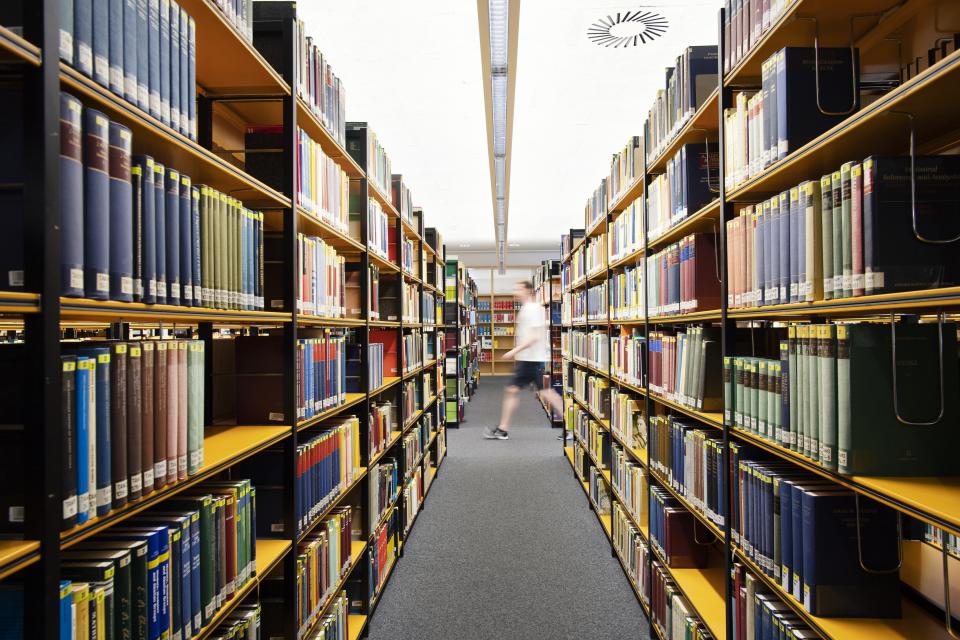 Innenansicht einer Bibliothek, in Regalen an der Seite stehen viele Bücher.