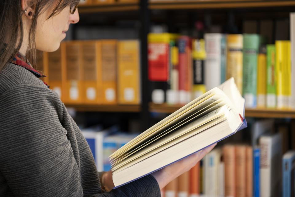 Eine Frau liest ein Buch, im Hintergrund Bücherregale