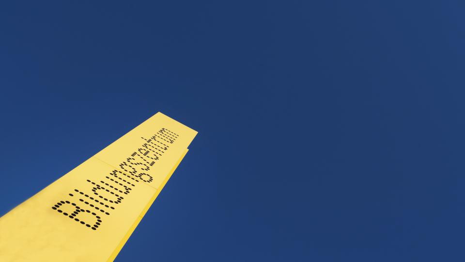 Ein gelbes Schild mit der Aufschrift "Bildungszentrum" ragt in einen blauen Himmel.